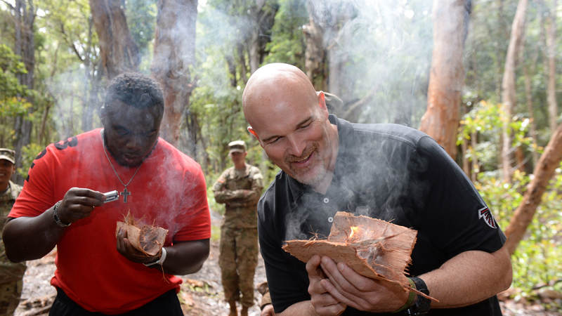 Soldiers (not pictured) teach Atlanta Falcons defensive tackle Grady Jarrett, left, and head coach Dan Quinn learn how to start a fire in a survival situation.