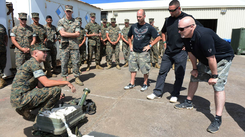 Atlanta Falcons kicker Matt Bryant, left, lineback Paul Worrilow, center, and head coach Dan Quinn learn the inner workings of a portable line charge, which is used to clear anti-personnel mines and wire obstacles.