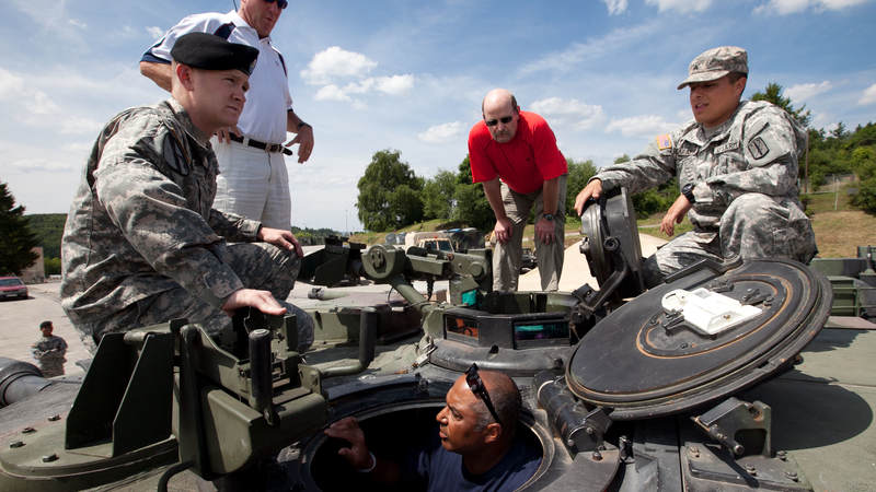 Two soldiers brief Carolina Panthers head coach John Fox (standing 2nd l), Minnesota Vikings head coach Brad Childress (standing 2nd r) and Cincinnati Bengals head coach Marvin Lewis (bottom in tank hatch) about the M1 Abrahms tank during a USO tour stop at Baumholder Army Garrison in Germany July 1, 2010.