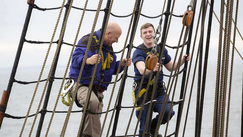 The Broadside creator Jeff Bacon has a laugh with a member of the USCGC Eagle crew as he climbs down the ship's riggings. USO Photo by Joseph Andrew Lee