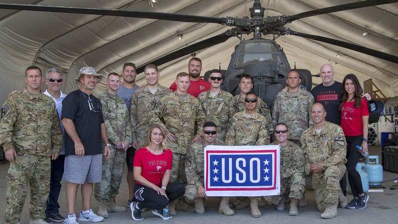 The Falcons crew poses with troops in front of an AH-64 Apache helicopter at Erbil Air Base, Iraq, during a USO tour.