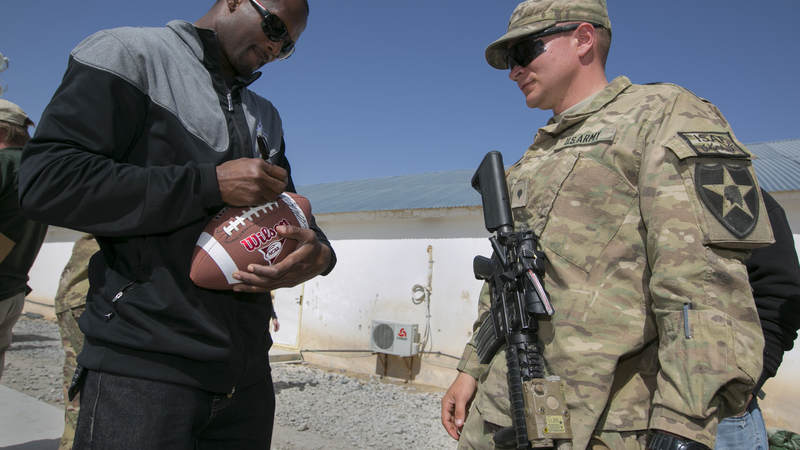 Then-Denver Broncos cornerback Champ Bailey autographs a football for a soldier stationed in the Middle East during a stop on a weeklong USO/NFL tour in March 2013.