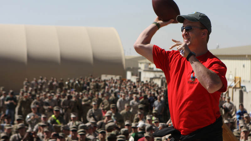 Peyton Manning tosses a pass into an audience of service members during 2013 trip to Camp Leatherneck, Afghanistan. Since teaming up in 1966, more than 180 NFL players, coaches, officials and executives have toured for the USO.