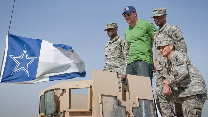 Dallas Cowboys tight end Jason Witten takes a photo with Cowboys fans on top of a vehicle proudly displaying a Cowboys flag, which Witten later autographed during a 2010 USO/NFL tour.