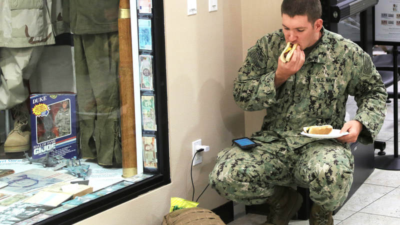 A Navy Seabee eats a hot dog and charges his phone Feb. 8 at USO Ontario during a short, late-night layover.