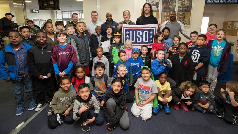 McAfee (in white left of banner), Adams, Coach Pagano, Castonzo and Jackson pose for a photo with the participants of an after-school athletics program at Fleet Activities Yokosuka naval base on Feb. 17.